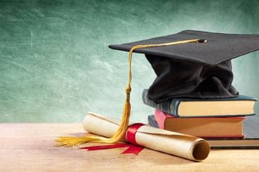 Graduation cap sitting on top of a small stack of books and next to a rolled diploma.