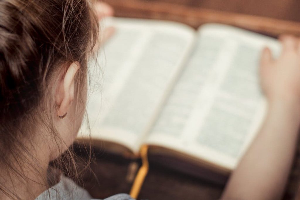 Young girl sitting down reading a Bible.