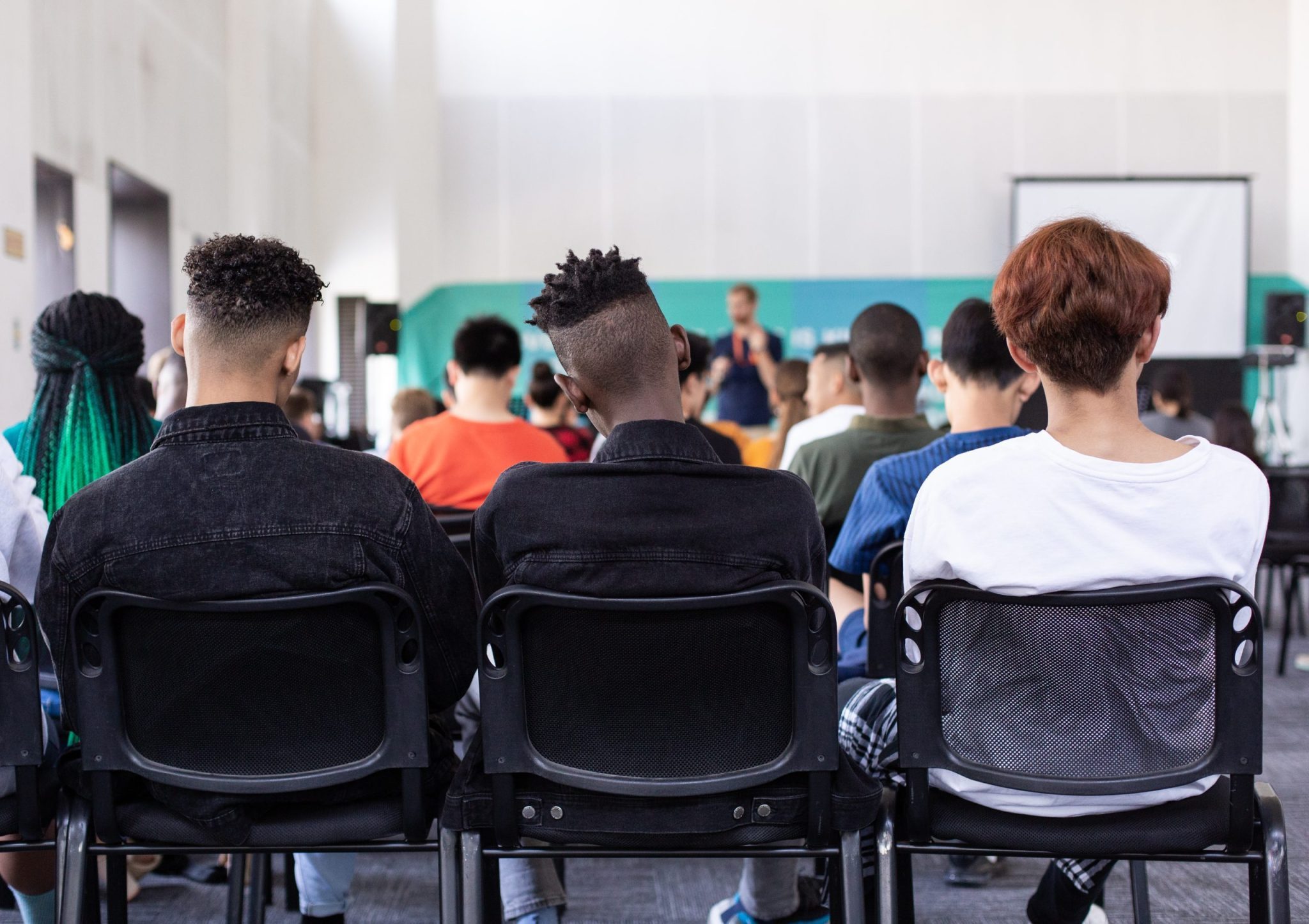 Back of students heads as they sit in a classroom listening to a teacher.