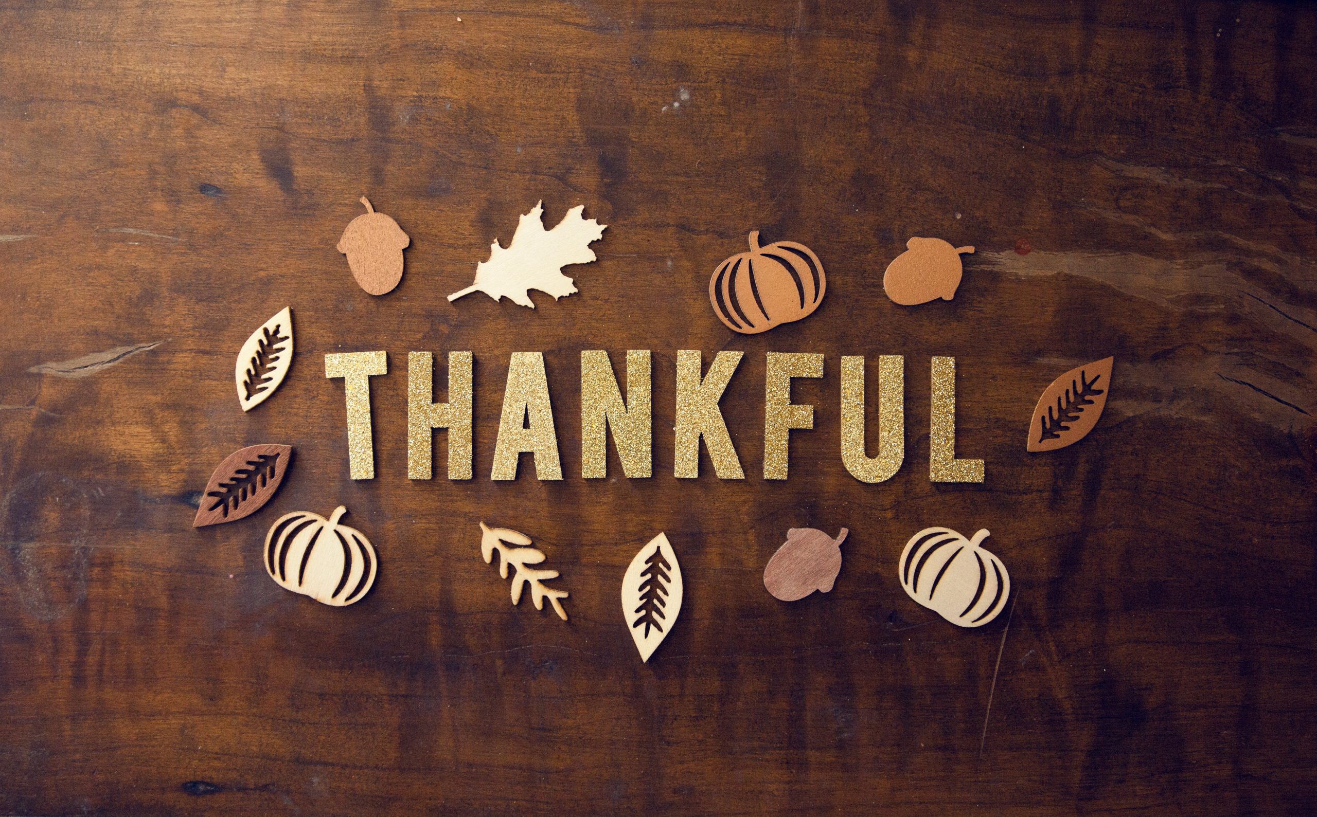 Fall leaves, acorns, and pumpkins scattered on table along with the word Thankful.