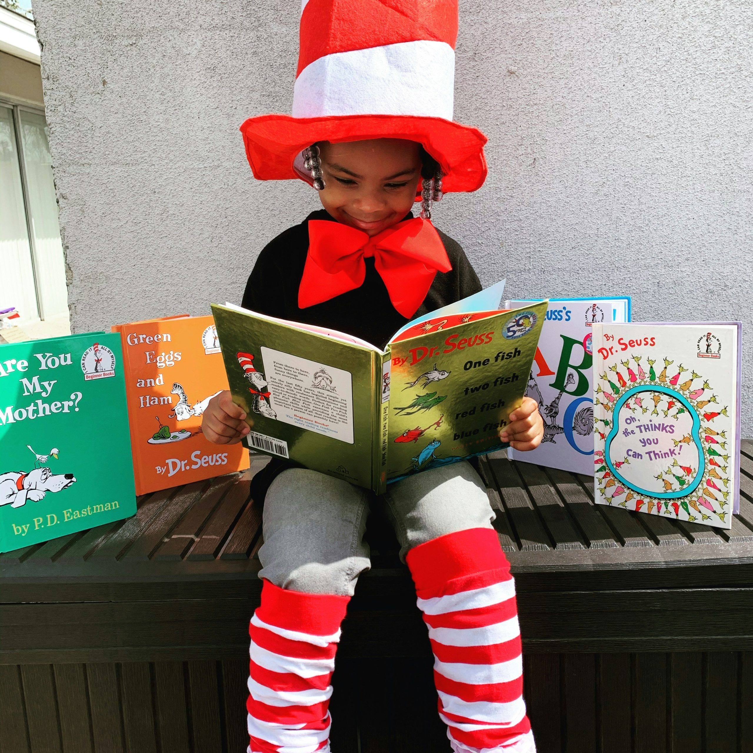 Child in Dr. Seuss outfit reading with books around them.